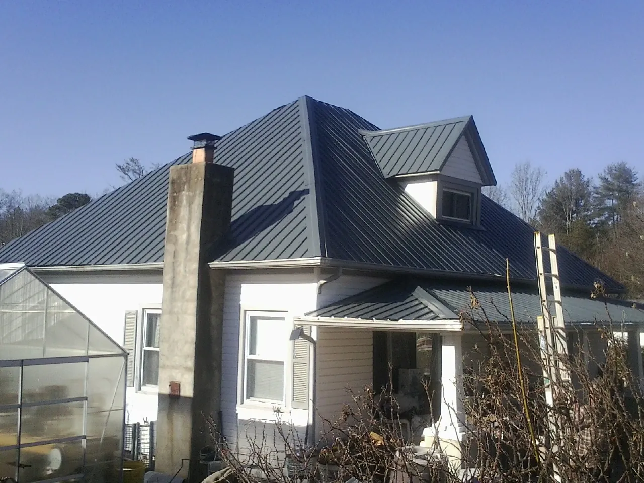 Dark blue standing seam metal roof on a white farmhouse with dormer — Slate & Tile Roof Repair by Roofing Brothers in Junction