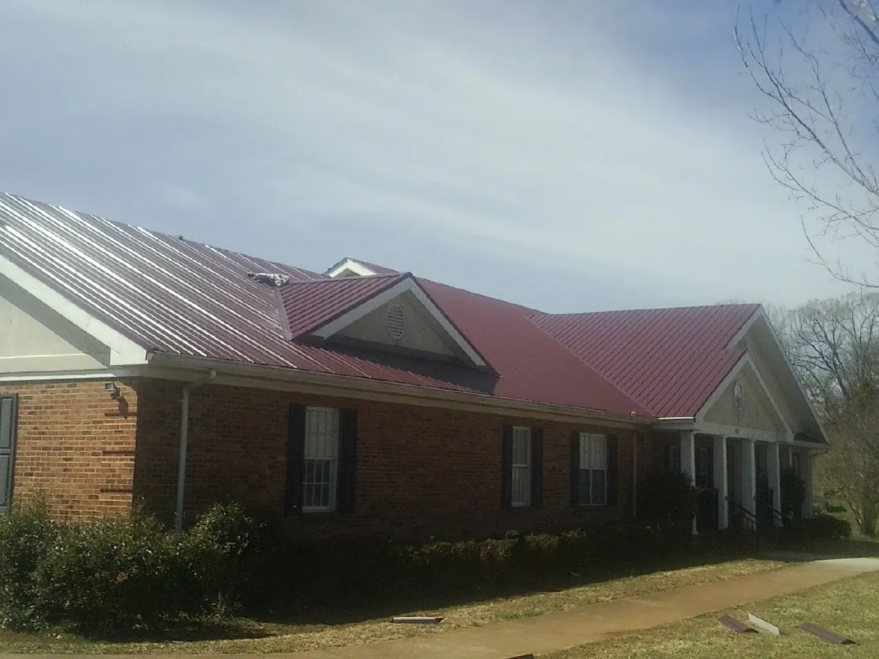 Red metal roof with gabled entries on a long brick building, from a Hail Damage Roof Repair job in Junction