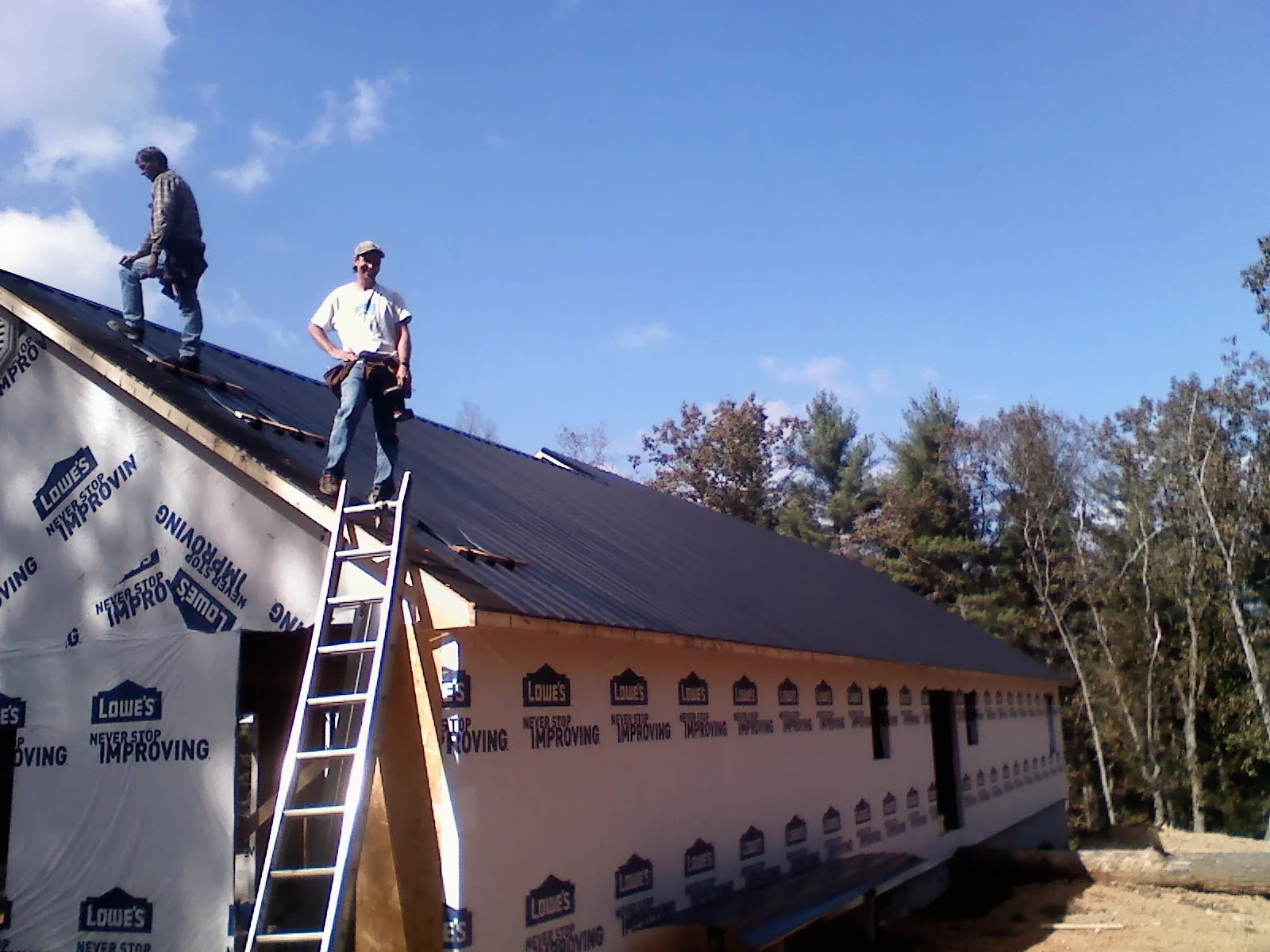 Two roofers standing on a long dark metal roof over a wrapped building in Junction