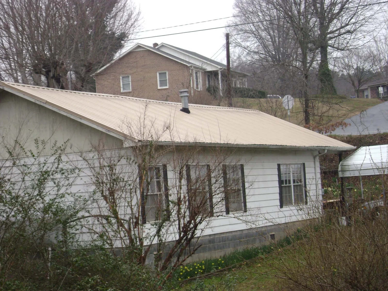 Tan metal roof on a white sided house set into a hillside — Commercial Roofing by Roofing Brothers in Junction